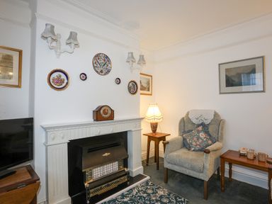 A sitting room with an armchair a fireplace decorative plates on the wall and a lamp on a side table at Bro Dawel in Beaumaris