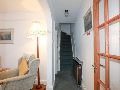 A hallway with stairs carpeted in dark green and a patterned armchair with a yellow cushion next to a standing lamp at Bro Dawel in Beaumaris