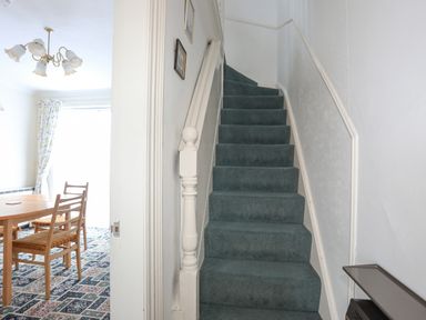 A carpeted staircase next to a dining area with a wooden table and chairs at Bro Dawel in Beaumaris
