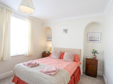 A bedroom with a double bed with coral bedspread and two side tables with lamps and flowers at Bro Dawel in Beaumaris