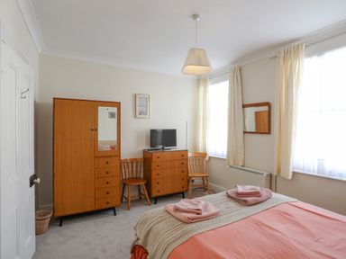 A bedroom with a bed towels on top wooden wardrobe chest of drawers two chairs and a television at Bro Dawel in Beaumaris