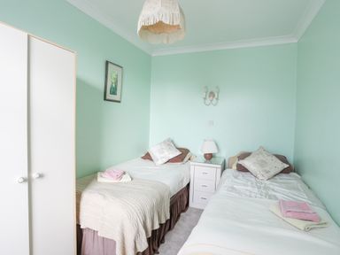 A bedroom with two single beds a wardrobe and a bedside table with a lamp at Bro Dawel in Beaumaris