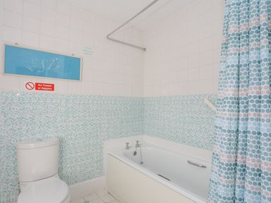 A bathroom with a toilet a bathtub with taps a shower curtain and tiled walls at Bro Dawel in Beaumaris