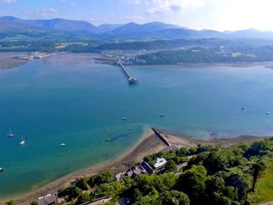 A coastal area with a pier extending into the water and hills in the background at Bro Dawel in Beaumaris