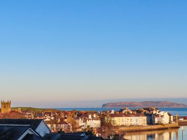 A coastal town with houses and a church near the water and an island in the distance at Bro Dawel in Beaumaris
