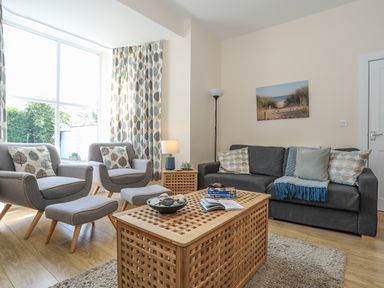 A living room with two armchairs and a sofa with cushions a wooden coffee table and a side table with a lamp and a floor lamp at Bryn Dale in Trearddur Bay