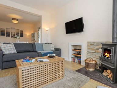 A living room with a grey sofa a wooden coffee table a wood burning stove and a wall mounted TV at Bryn Dale in Trearddur Bay