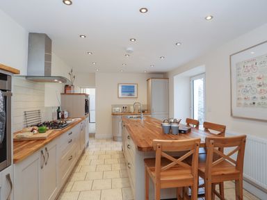 A kitchen with wooden countertops a kitchen island with wooden chairs and a framed bicycle poster on the wall at Bryn Dale in Trearddur Bay
