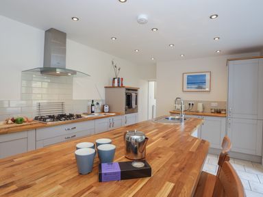 A kitchen with wooden countertops a gas stove a stainless steel kettle four cups a sink and gray cabinets at Bryn Dale in Trearddur Bay