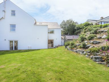 A white house with a lawn and a garden with stone terraces at Bryn Dale in Trearddur Bay