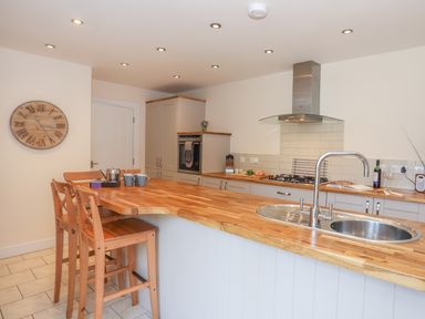 A kitchen with wooden countertops a sink stove and bar stools at Bryn Dale in Trearddur Bay