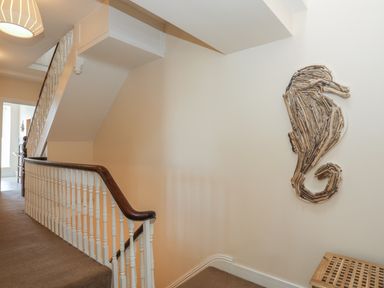 A staircase with a wooden handrail and white balusters next to a wall with a driftwood seahorse decoration and a small wooden bench at Bryn Dale in Trearddur Bay
