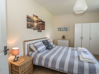 A bedroom with a double bed with striped bedding two bedside tables with lamps a chest of drawers and a wardrobe at Bryn Dale in Trearddur Bay