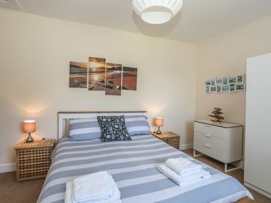 A bedroom with a double bed striped bedding bedside tables with lamps a dresser and wall art at Bryn Dale in Trearddur Bay