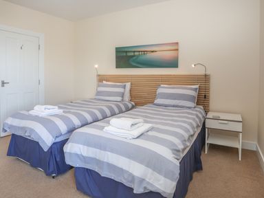 A bedroom with two single beds with striped bedding and a nightstand at Bryn Dale in Trearddur Bay