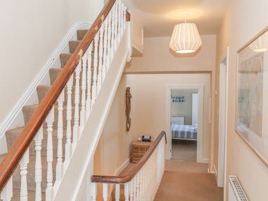 A hallway with carpeted stairs a wooden banister a light fixture and a view into a bedroom at Bryn Dale in Trearddur Bay