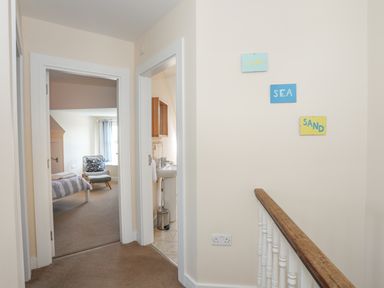 A hallway with doors leading to a bedroom and bathroom and signs reading sun sea sand at Bryn Dale in Trearddur Bay