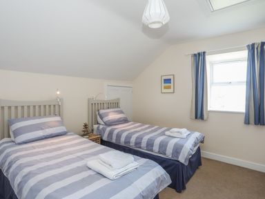 A bedroom with two single beds with striped bedding and towels on top at Bryn Dale in Trearddur Bay