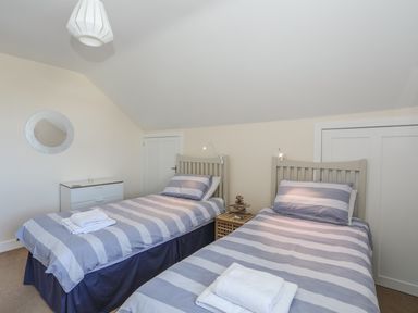 A bedroom with two single beds striped bedding bedside table and chest of drawers at Bryn Dale in Trearddur Bay
