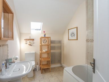 A bathroom with a sink toilet wooden shelving heated towel rail and bathtub at Bryn Dale in Trearddur Bay