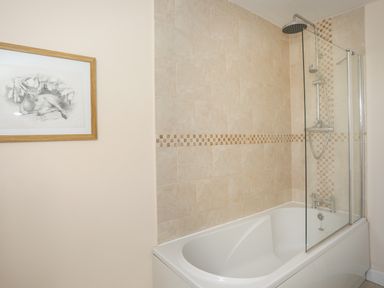 A bathroom with a bathtub shower and a framed picture on the wall at Bryn Dale in Trearddur Bay