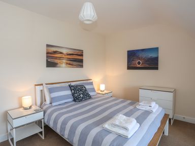 A bedroom with a double bed with striped bedding two bedside tables with lamps and a chest of drawers at Bryn Dale in Trearddur Bay