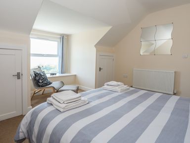 A bedroom with a bed covered by a striped duvet and towels on it a chair with a footrest near a window and a decorative mirror on the wall at Bryn Dale in Trearddur Bay