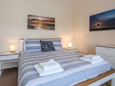 A bedroom with a double bed striped bedding bedside tables with lamps and wall pictures at Bryn Dale in Trearddur Bay