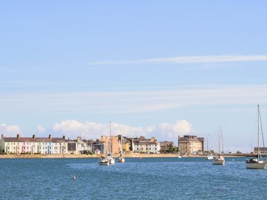 A seafront with boats anchored in the water and buildings along the shore at Bryn Tegid in Beaumaris