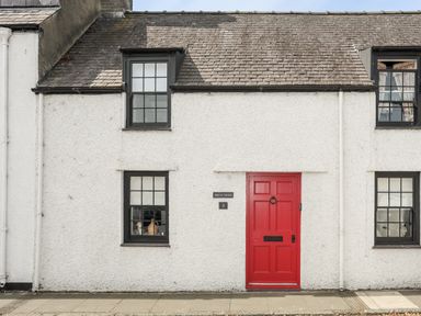 A white house exterior with black window frames and a red door at Bryn Tegid in Beaumaris