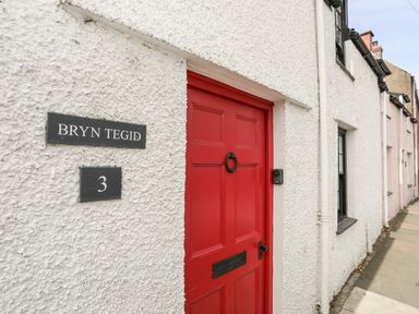 A white textured exterior wall with a red door and house sign reading Bryn Tegid number 3 in Beaumaris