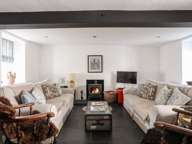 A living room with two beige sofas a wood stove and a television at Bryn Tegid in Beaumaris