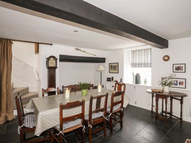 A dining room with a long wooden table covered with a polka dot tablecloth and wooden chairs around it at Bryn Tegid in Beaumaris
