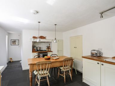 A kitchen with a wooden dining table and chairs two hanging lights and kitchen appliances at Bryn Tegid in Beaumaris