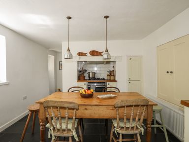 A kitchen with a wooden table and chairs a stove with cooking utensils and hanging lights at Bryn Tegid in Beaumaris