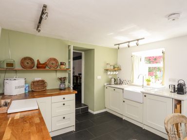 A kitchen with wooden countertops white cabinets and a window with curtains at Bryn Tegid in Beaumaris