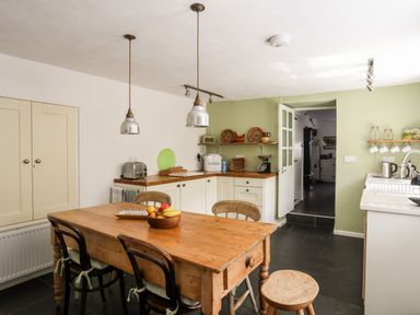 A kitchen with a wooden dining table and chairs a toaster on the counter and shelves with kitchen items at Bryn Tegid in Beaumaris