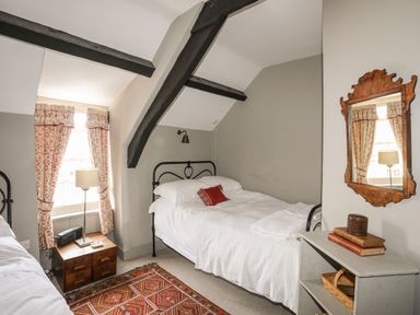 A bedroom with two single beds wooden nightstand with lamp and radio and a wall mirror at Bryn Tegid in Beaumaris