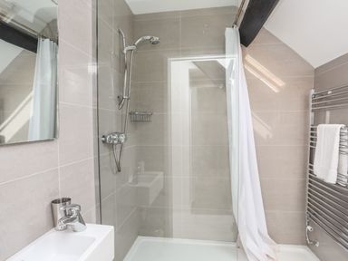 A bathroom with a shower area a sink a mirror a towel rack with towels and a shower curtain at Bryn Tegid in Beaumaris