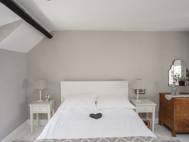 A bedroom with a white bed framed by two white bedside tables with lamps and a wooden dresser with a mirror at Bryn Tegid in Beaumaris