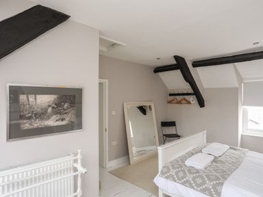 A bedroom with a white bed and folded towels on a blanket a black chair a large floor mirror a painting on the wall and exposed black ceiling beams at Bryn Tegid in Beaumaris