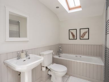 A bathroom with a sink, toilet, bathtub, mirror, two framed pictures and a skylight at Bryn Tegid in Beaumaris