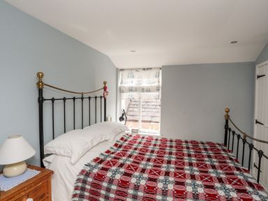 A bedroom with a black and brass metal bed frame white pillows a red and white patterned blanket a wooden bedside table with a lamp and a window with a ship-patterned blind at Bryn Tegid Beaumaris