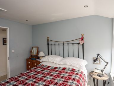 A bedroom with a bed with a red patterned blanket and white pillows next to wooden and round side tables with lamps at Bryn Tegid in Beaumaris