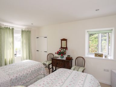 A bedroom with two single beds covered with floral bedspreads two wooden chairs with cushions a wooden side table with a vase of flowers and a mirror on the wall at Bryn Tegid in Beaumaris