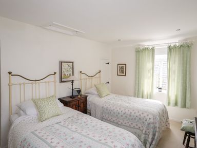A bedroom with two single beds green pillows wooden nightstand and green curtains at Bryn Tegid in Beaumaris
