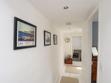 A hallway with framed pictures on the wall and a chest at the end at Bryn Tegid in Beaumaris