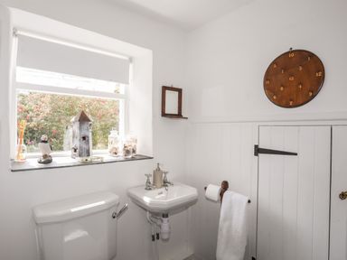A bathroom with a toilet sink towel rack and window with decorations at Bryn Tegid in Beaumaris