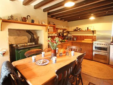 A kitchen with a wooden dining table and chairs a stove flowers on the table and wooden cabinets at Buck Cottage in Red Wharf Bay