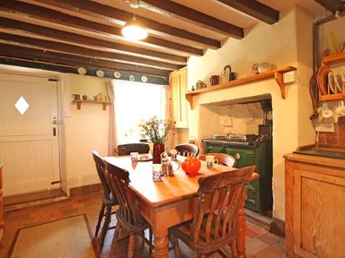 A kitchen with wooden dining table and chairs a green stove and shelves with crockery at Buck Cottage in Red Wharf Bay